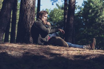 Side view of resting hiker in forest sitting against tree.