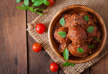 Meatballs in sweet and sour tomato sauce and basil in a wooden bowl. Top view