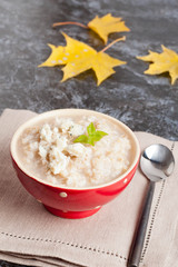 Oatmeal porridge with cheese in bowl and autumn leaves on black