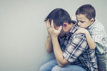 sad son hugging his dad near wall