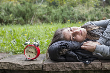 Young woman with red alarm clock in the park