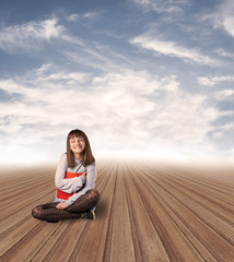 young woman alone hugging a book sitting on a wooden floor