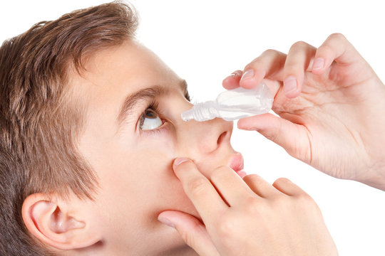 Young boy applying eye drop. On white background