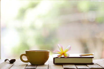 Yellow cup and notebook with frangipani flower