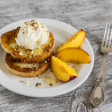 French toast with ice cream and honey on a white plate, on bright wooden surface