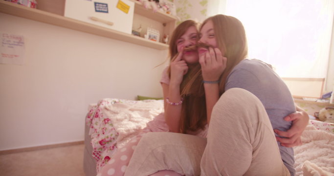 Girls on a bed holding each other's hair as moustaches