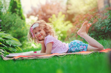 Obraz na płótnie Canvas happy child girl reading on summer vacation in sunny garden