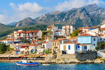 Papier Peint photo Île Typical Greek fishing boat in Kokkari bay with town houses in background, Samos island, Greece
