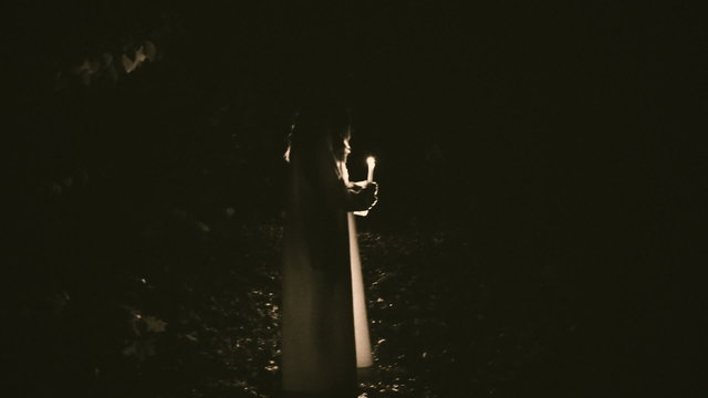 Silhouette of a witch with a candle in a dark forest