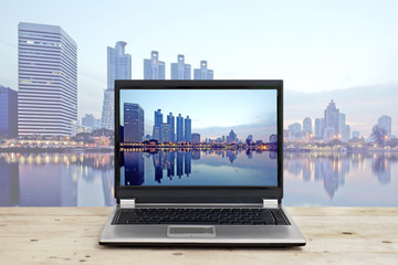 laptop on wooden table with cityscape high building background
