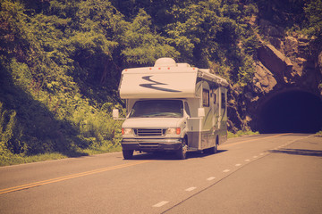 Retro filter style image of RV camper driving down highway with rock tunnel