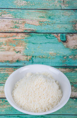 Grated cheese in white bowl over wooden background