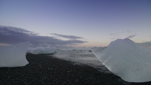 Icebergs washed up the black lava beach near the Jokulsarlon glacier lagoon in Iceland during a sunset.