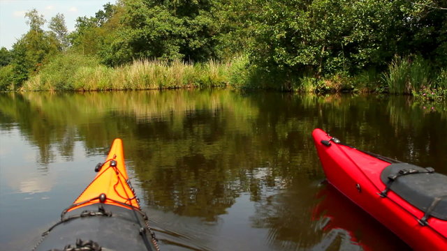 On board shot of a red and orange kayak paddling on a canal in a nature reserve. 