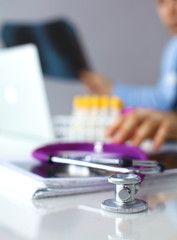 A medical stethoscope near a laptop on a wooden table, on white