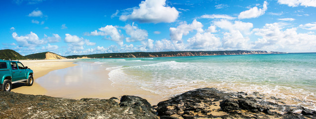 View of beach cove with rock platform and four wheel drive on a sunny day. Rainbow Beach, Queensland, Australia.
