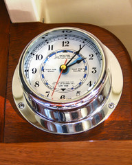 Chrome marine tide clock mounted to wood on a ferry.