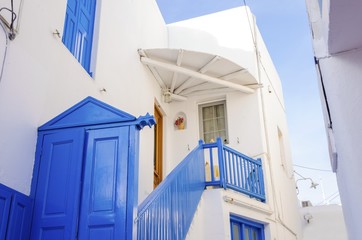 A very traditional alley view of the architecture in Chora, on the greek island Mykonos, Greece. A blue door, fence and windows of a whitewashed house against the blue sky. © f8grapher