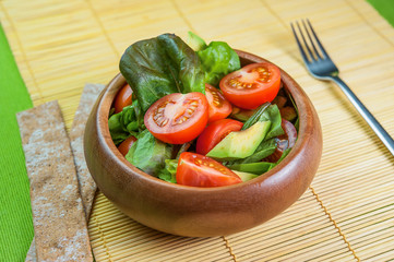 Fresh vegetable salad in wooden bowl on bamboo napkin with crispbread