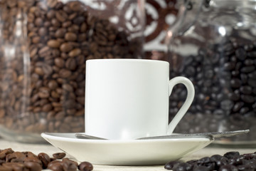 White coffee cup in front of glass pots with different types of roasted coffee beans