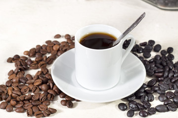 Coffee cup over a saucer, beside natural roasted and torrefacto coffee beans