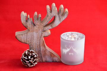 red Christmas background with three tea candle holders decorated with a wooden reindeer and pine apple