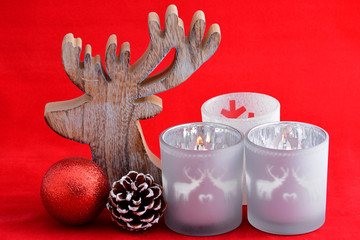red Christmas background with three tea candle holders decorated with a wooden reindeer , pine apple and christmas ball