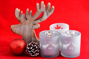 red Christmas background with three tea candle holders decorated with a wooden reindeer , pine apple and christmas ball