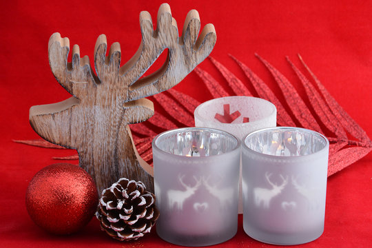 red Christmas background with three tea candle holders decorated with a wooden reindeer , pine apple and christmas ball - Powered by Adobe