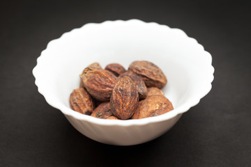 Organic Inknut or Harr (Terminalia chebula) in white ceramic bowl on dark background.