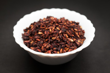 Organic Dried Pomegranate seeds (Punica granatum) in white ceramic bowl on dark background.