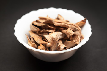 Organic Sour dried mango or Aamchur or Amchoor (Mangifera indica) in white ceramic bowl on dark background.