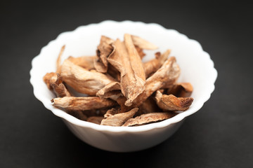 Organic Sour dried mango or Aamchur or Amchoor (Mangifera indica) in white ceramic bowl on dark background.