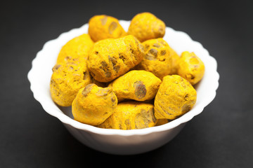 Organic Round Turmeric or Haldi (Curcuma longa) in white ceramic bowl on dark background.