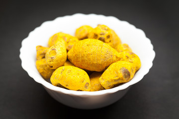 Organic Round Turmeric or Haldi (Curcuma longa) in white ceramic bowl on dark background.