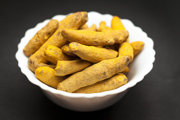 Organic Long Turmeric or Haldi (Curcuma longa) in white ceramic bowl on dark background.