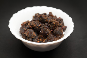Organic Indian bdellium or Guggul resin (Commiphora wightii) in white ceramic bowl on dark background.