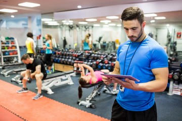 Fototapeta na wymiar Handsome trainer using tablet in weights room
