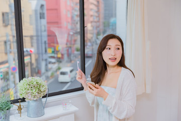 歯磨きをしながら携帯電話を操作するパジャマ姿の女性
