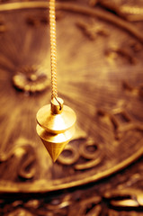 a gold pendulum over astrological background