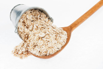 Bucket of rolled oats crumbles in the a wooden spoon