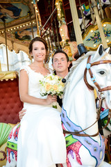 happy young married couple bride and groom playing on merry-go-round during their romantic wedding day