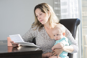 Mother holding baby  and typing on laptop computer in kitchen.