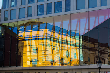 Old house reflected in  glass windows of modern  skyscraper.
