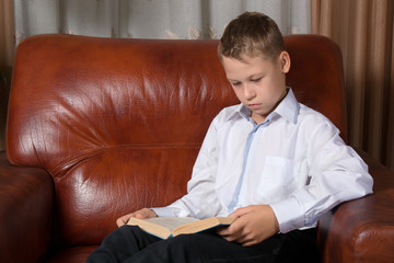 Young boy reading book on sofa at home © bayurov
