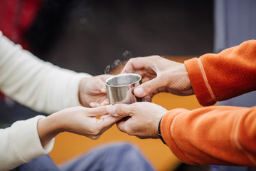Womans and mens hands holding hot cup of tea in forest camp