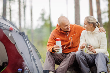 Two campers talking to each other and drinking tea by a tent in