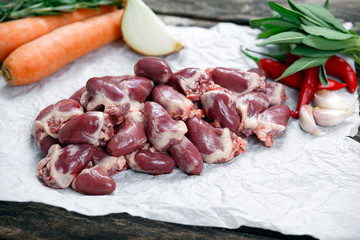 Raw Duck hearts on crumpled paper, decorated with vegetables. on old wooden table.