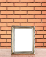 Fototapeta premium Old empty frame standing on table on brick wall background