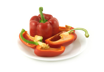 One whole and some sliced red ripe bell peppers on a plate isolated over white closeup